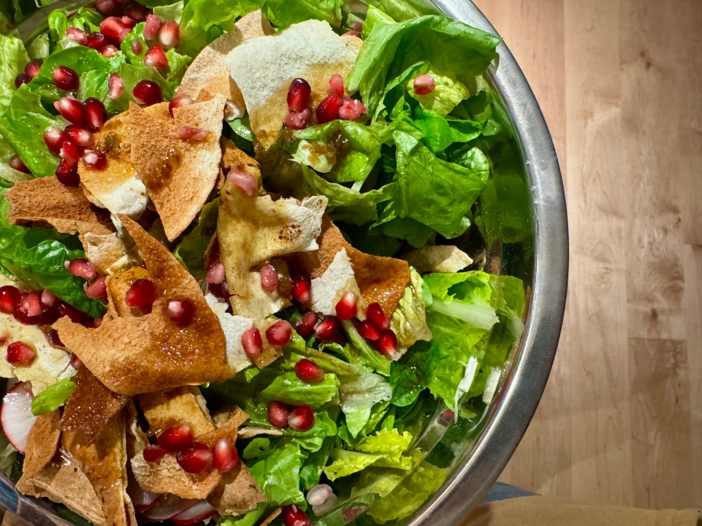 Salade verte avec des morceaux de pita, des graines de grenade et une vinaigrette.